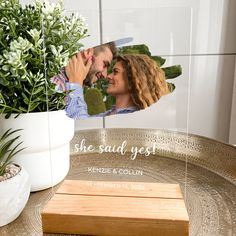 a couple kissing in front of a vase with greenery and a wooden cutting board