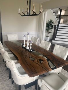 a large wooden table surrounded by white chairs and chandeliers in a dining room