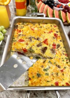 a close up of a pan of food on a table with fruit in the background