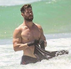 a shirtless man in the ocean with a wet suit around his waist holding a towel