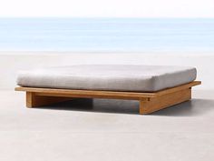 a wooden bench sitting on top of a cement floor next to the ocean and sky