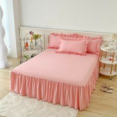 a pink bed with ruffles on it in a white and wood floored room