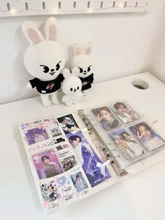 two stuffed animals sitting on top of a white desk next to a binder filled with photos