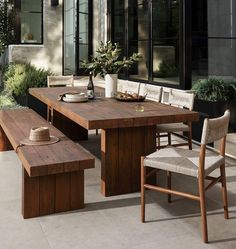 a wooden table with benches and chairs around it in front of a building that has large windows