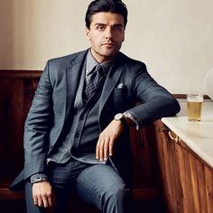 a man in a suit sitting on a bench next to a glass of beer and looking at the camera