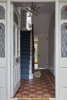 an open door leading to a hallway with blue stairs and patterned tile flooring on the ground