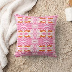 a pink and orange pillow sitting on top of a fluffy white rug next to a blanket