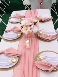 the table is set with pink napkins and gold place settings, along with flowers in a vase