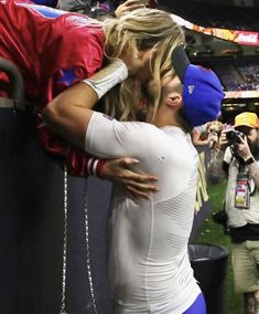 two women kissing each other in front of a crowd at a baseball game with cameras around them