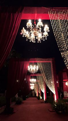 an outdoor wedding venue decorated with red drapes, chandeliers and white lights