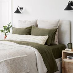 a bed with two lamps on the wall above it and a potted plant next to it