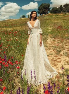 a woman in a white dress standing in a field full of wildflowers and trees