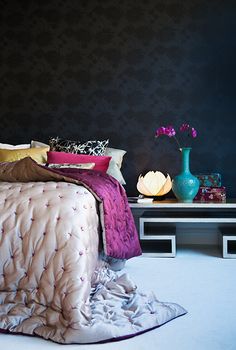 a bed sitting in a bedroom next to a table with a vase on top of it