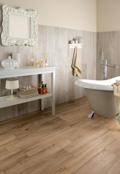 a bath tub sitting next to a white sink in a bathroom on top of a hard wood floor