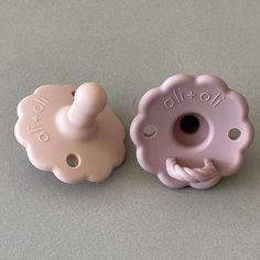 two baby pacifiers sitting next to each other on a gray counter top, one pink and the other light pink