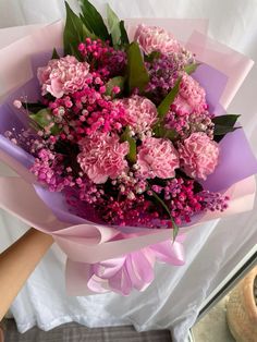 a bouquet of pink carnations and lilacs is held by someone's hand