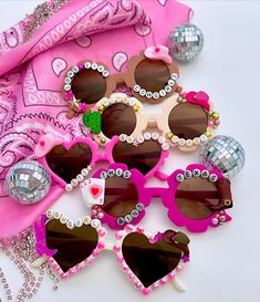 several pairs of heart shaped sunglasses are laying on a pink scarf and some disco balls