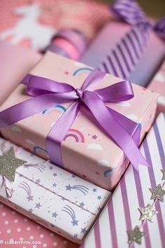 three wrapped presents with purple ribbons and stars on pink wrapping paper next to each other