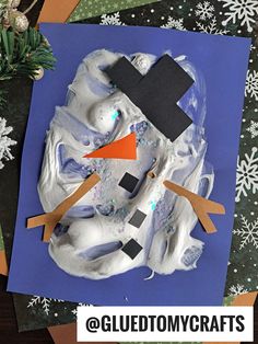 a snowman made out of paper on top of a blue surface with white snowflakes