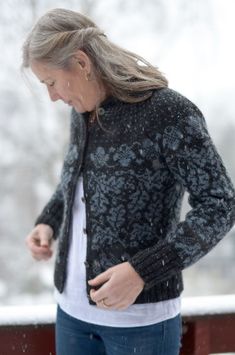 a woman standing outside in the snow looking at her cell phone while wearing a black cardigan