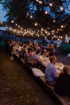 many people are sitting at long tables with lights strung over them and there is no image here to provide a caption for