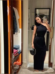 a woman taking a selfie in front of a mirror wearing a black dress and holding a purse