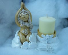 a candle sitting next to a statue on top of snow covered ground with clouds in the background