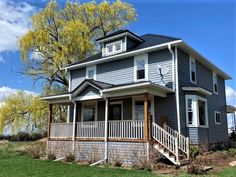 a blue house with white trim and porches on the front lawn, under a tree