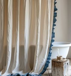 a white bath tub sitting under a window next to a wooden stool and shower curtain