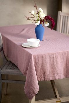 a blue vase with white flowers sits on a pink tablecloth next to a plate