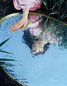 a person's feet sticking out of the water in front of grass and plants