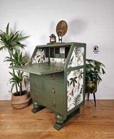 an old fashioned green desk with plants in the corner and a potted plant next to it