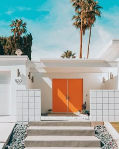 an orange door in front of a white house with steps leading up to it and palm trees