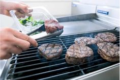 the hamburgers are being cooked on the grill by someone using tongs to stir them