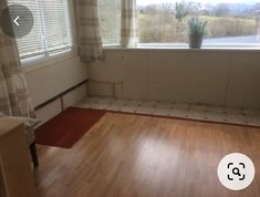 an empty room with wooden floors and a large window overlooking the countryside outside, in front of a curtained window