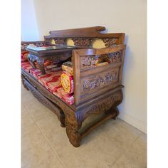 an ornate wooden bed frame with red and gold pillows on it's sides, sitting against a white wall