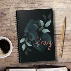 an open book with the word pray on it next to a cup of coffee and pen