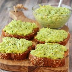 four pieces of bread with guacamole spread on them and a bowl of dip in the background