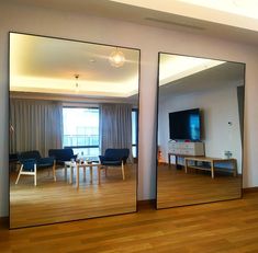 two large mirrors are reflecting the living room and dining area in this modern apartment with wood flooring