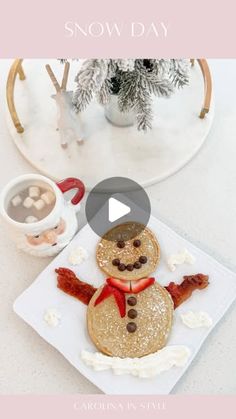 a snowman cookie sitting on top of a white plate next to a cup of coffee