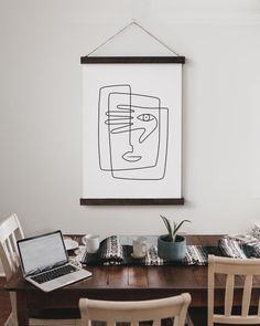 a wooden table topped with a laptop computer next to a wall mounted art work piece