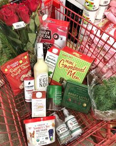 a red shopping cart filled with lots of food and drinks next to some flowers on the ground