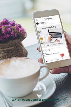 a person holding a cell phone in front of a cup of coffee