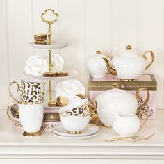 there is a white and gold tea set on the shelf next to other dishes, cups and saucers