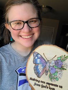 a woman wearing glasses and holding a wooden plaque with a butterfly on it that says nothing can separate us from god's love