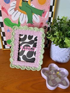 a pink and green frame sitting on top of a wooden table next to a potted plant