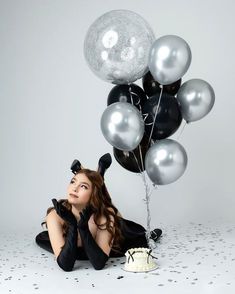 a woman laying on the floor with balloons and cake in front of her, posing for a photo