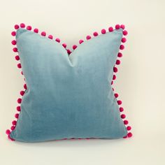 a blue pillow with pink pom - poms on the front and back sides