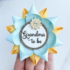 a hand holding a blue and yellow ribbon with the words grandma to be on it