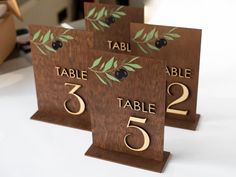 three wooden table numbers with olive leaves on them